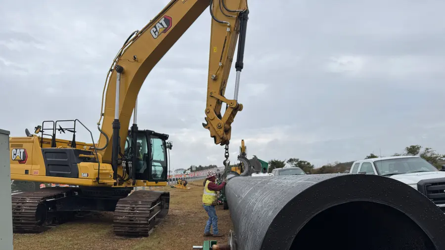An excavator handling a section of large-diameter pipe on the right-of-way