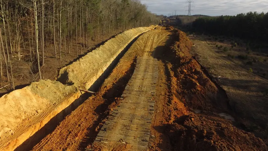 A graded pipeline right-of-way running cross-country toward transmission towers