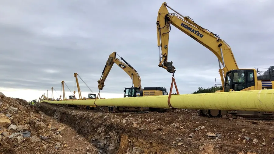 A row of sidebooms carrying welded pipe along the right-of-way
